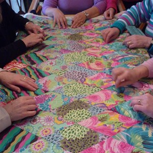 A fantastically coloured quilt being stretched Photo of hands working on a quilt